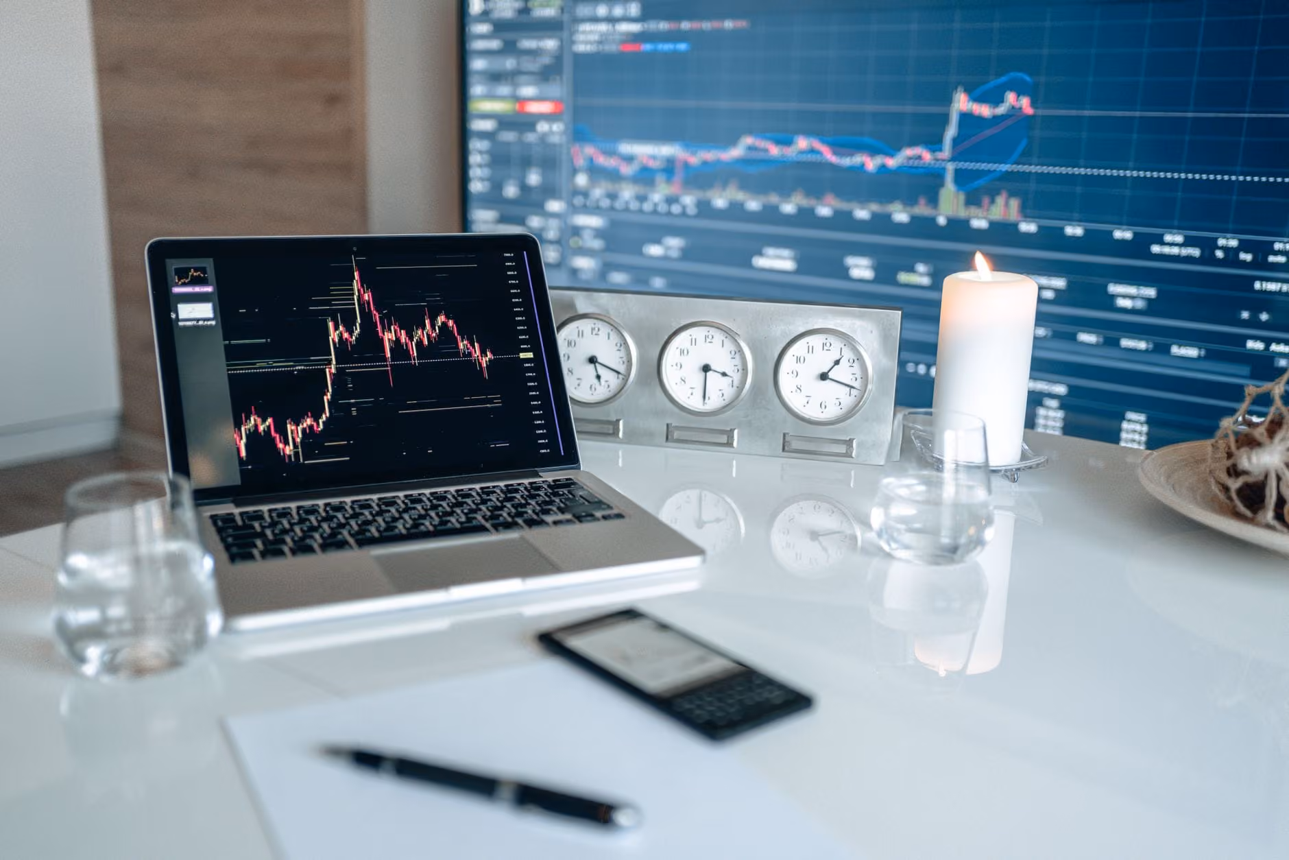 A modern workspace featuring financial charts and multiple clocks on a white table, ideal for trading.