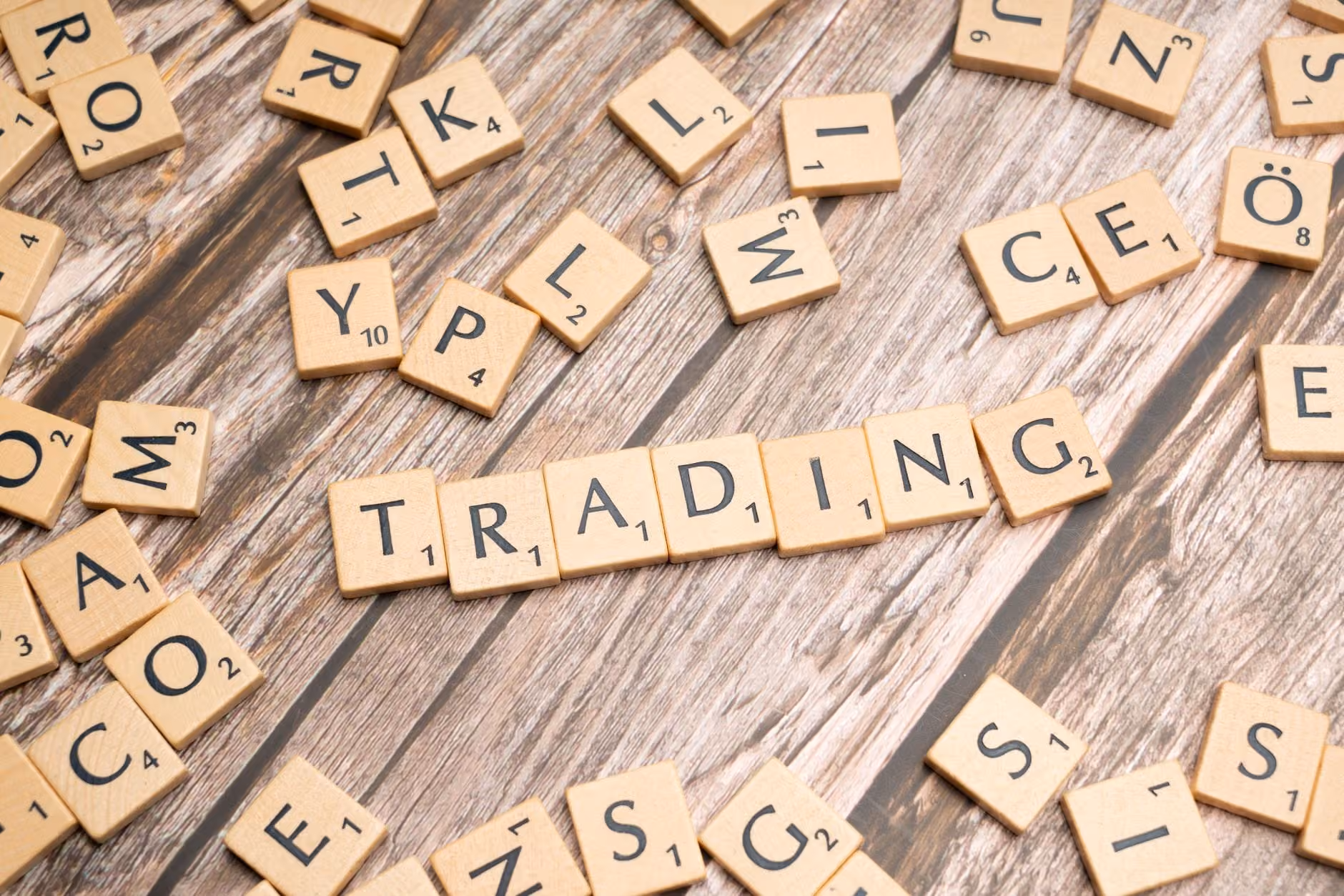Wooden Scrabble tiles spelling 'TRADING' against a rustic wood background.
