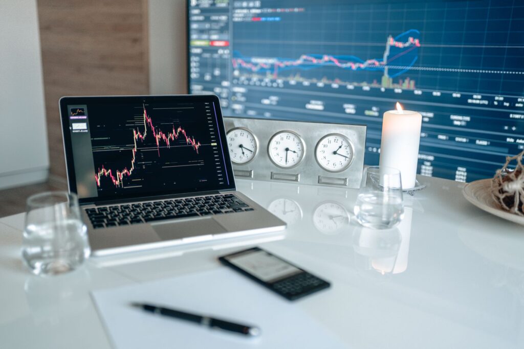 A modern workspace featuring financial charts and multiple clocks on a white table, ideal for trading.